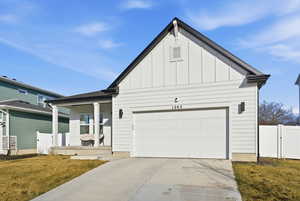 Modern farmhouse style home with board and batten siding, a porch, driveway, and a gate