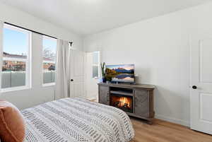 Bedroom with light wood-style flooring and a lit fireplace