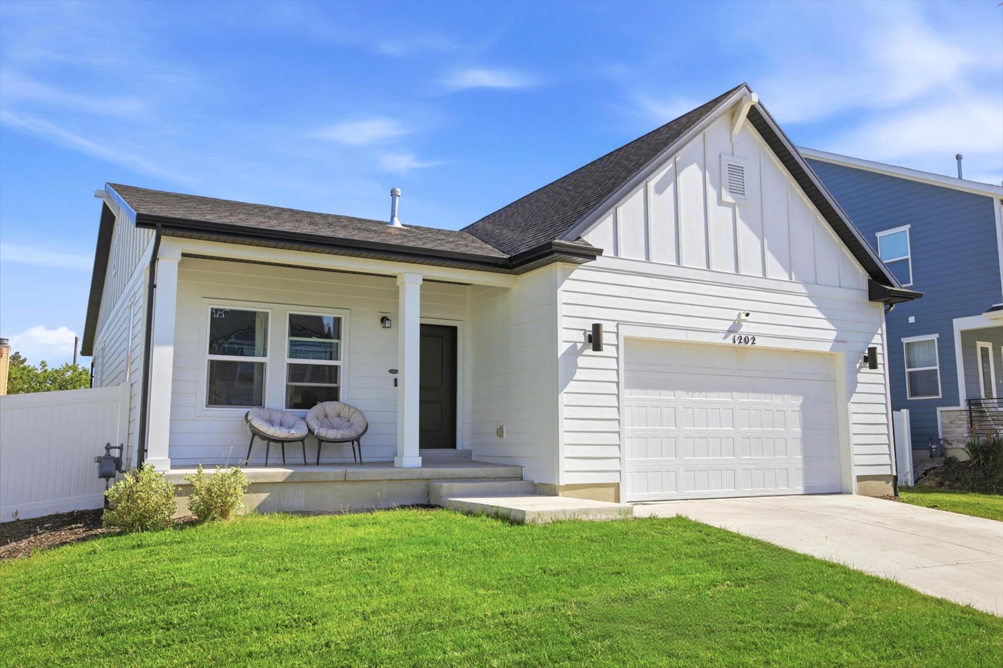 Modern farmhouse exterior featuring white horizontal siding, a prominent gable roofline, an attached single-car garage, and a covered front porch with white columns