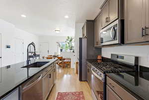 Kitchen with stainless steel appliances, dark stone countertops, a textured ceiling, light wood-style flooring, and recessed lighting