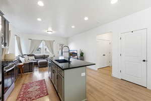 Kitchen with open floor plan, a center island with sink, gas stove, light wood-style floors, and recessed lighting