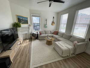 Living room with wood finished floors, ceiling fan, a fireplace, and ornamental molding
