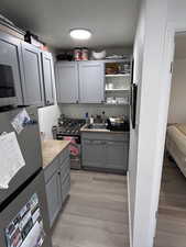 Kitchen featuring gray cabinetry, appliances with stainless steel finishes, light countertops, light wood-type flooring, and a textured wall