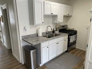 Kitchen with gas range, white cabinetry, light stone counters, and dark wood-type flooring