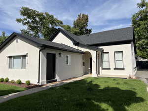 View of front of house featuring stucco siding, a front yard, and a shingled roof
