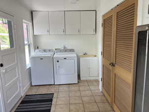Washroom featuring washer and dryer, cabinet space, a heating unit, and light tile patterned floors