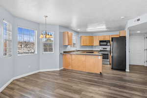 Kitchen featuring a peninsula, black appliances, a chandelier, hanging light fixtures, and dark countertops