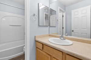 Bathroom with vanity, washtub / shower combination, and dark wood-type flooring
