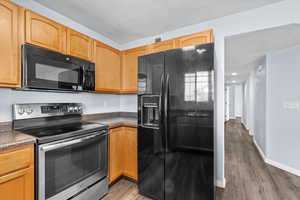 Kitchen featuring dark countertops, black appliances, a textured ceiling, and light wood-style floors