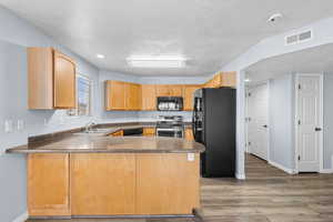 Kitchen featuring a peninsula, black appliances, dark countertops, light wood finished floors, and a textured ceiling