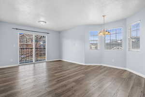 Empty room with a textured ceiling, wood finished floors, and a chandelier