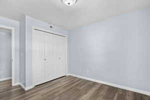 Unfurnished bedroom with a textured ceiling, a closet, and wood finished floors