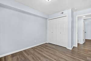 Unfurnished bedroom featuring a textured ceiling, a closet, and wood finished floors
