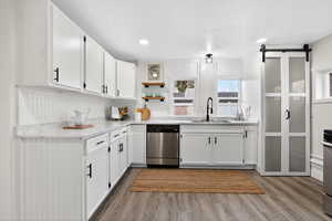 Kitchen with a barn door, white cabinetry, open shelves, stainless steel dishwasher, and dark wood-type flooring