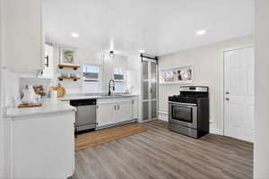 Kitchen with a barn door, appliances with stainless steel finishes, white cabinetry, open shelves, and recessed lighting