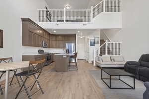 Kitchen with open floor plan, stainless steel appliances, light countertops, a high ceiling, and an island with sink