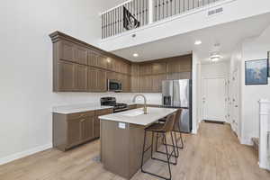 Kitchen featuring a breakfast bar, stainless steel appliances, light wood-style floors, recessed lighting, and a kitchen island with sink