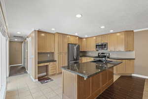 Kitchen featuring crown molding, a kitchen island with sink, stainless steel appliances, dark stone countertops, and decorative backsplash