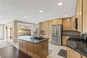 Kitchen with appliances with stainless steel finishes, a kitchen island with sink, a textured ceiling, ornamental molding, and recessed lighting