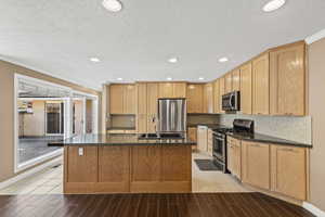 Kitchen with light brown cabinetry, stainless steel appliances, recessed lighting, tasteful backsplash, and a kitchen island with sink