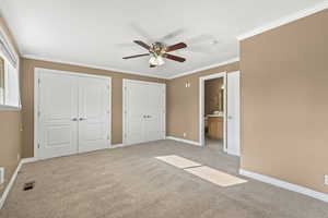 Unfurnished bedroom with two closets, ornamental molding, light colored carpet, a ceiling fan, and ensuite bathroom
