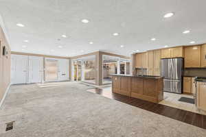 Kitchen featuring open floor plan, a textured ceiling, appliances with stainless steel finishes, an island with sink, and recessed lighting