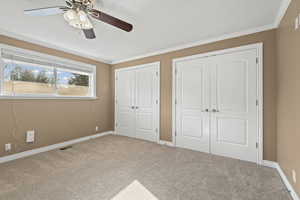 Unfurnished bedroom with two closets, carpet, crown molding, and a ceiling fan