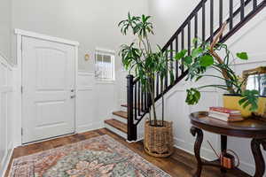 Entrance foyer featuring a decorative wall, wainscoting, stairway, and dark wood finished floors