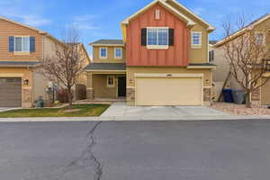 View of front of home featuring board and batten siding, stone siding, concrete driveway, a garage, and stucco siding