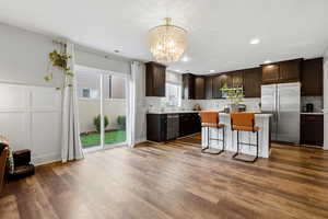Kitchen with dark brown cabinetry, a breakfast bar area, appliances with stainless steel finishes, light countertops, and a decorative wall