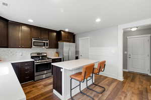 Kitchen featuring dark brown cabinets, appliances with stainless steel finishes, a breakfast bar area, a center island, and a wainscoted wall