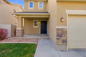 Doorway to property featuring a garage, stone siding, a porch, stucco siding, and a shingled roof