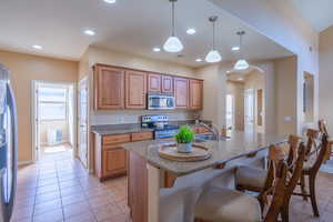 Kitchen featuring brown cabinets, dark stone countertops, stainless steel appliances, light tile patterned flooring, and a breakfast bar area