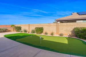 Fenced backyard featuring an area to practice putting