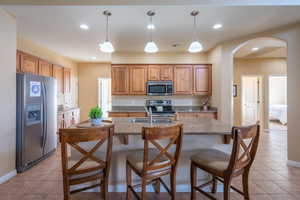 Kitchen featuring appliances with stainless steel finishes, a breakfast bar area, brown cabinets, light tile patterned floors, and recessed lighting