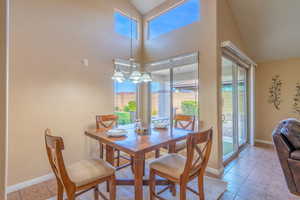Dining room with healthy amount of natural light, light tile patterned floors, a chandelier, and high vaulted ceiling