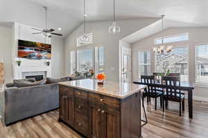 Kitchen featuring light stone countertops, dark brown cabinets, decorative light fixtures, a kitchen island, and light wood-type flooring