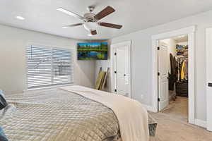 Bedroom with light colored carpet, a walk in closet, and a ceiling fan