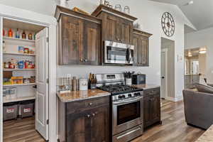 Kitchen with appliances with stainless steel finishes, light stone countertops, dark brown cabinetry, and high vaulted ceiling