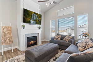 Living area with wood finished floors, a fireplace with flush hearth, a ceiling fan, and high vaulted ceiling