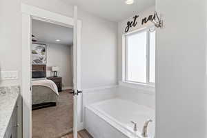 Ensuite bathroom featuring vanity, a garden tub, light colored carpet, and recessed lighting