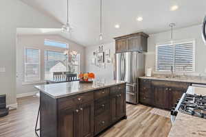 Kitchen featuring dark brown cabinets, freestanding refrigerator, light stone countertops, pendant lighting, and lofted ceiling