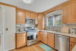 Kitchen with appliances with stainless steel finishes, light countertops, light wood finished floors, and light brown cabinetry