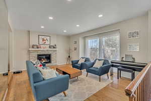Living room with a stone fireplace, light wood-type flooring, and recessed lighting