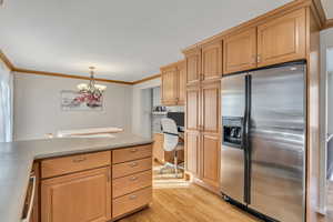 Kitchen featuring stainless steel fridge with ice dispenser, ornamental molding, decorative light fixtures, light wood-style flooring, and light countertops
