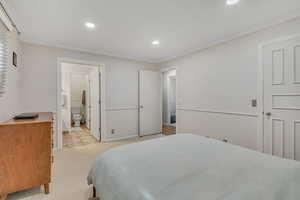 Bedroom with light colored carpet, recessed lighting, ornamental molding, and ensuite bath