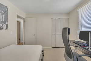 Bedroom with an office area, light colored carpet, and a closet