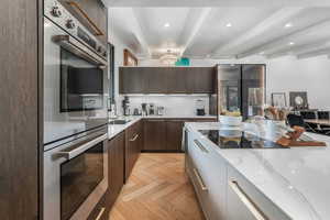 Kitchen with modern cabinets, stainless steel double oven, light stone countertops, dark brown cabinetry, and recessed lighting