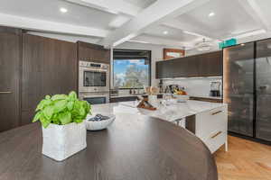 Kitchen with modern cabinets, dark brown cabinets, beam ceiling, recessed lighting, and light stone countertops