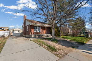 Bungalow featuring a chimney, brick siding, concrete driveway, and a gate